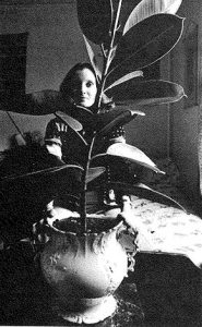 Lori O'Connor sits behind her tall rubber plant.