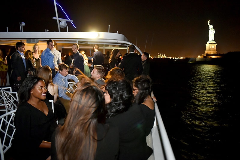Guests mingle on the top deck as Fordham's 2017 Young Alumni Yacht Cruise passes within view of the Statue of Liberty. 