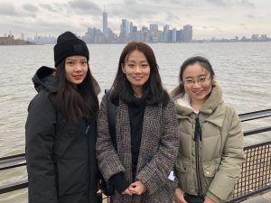 Three students stand in front of the Manhattan skyline.
