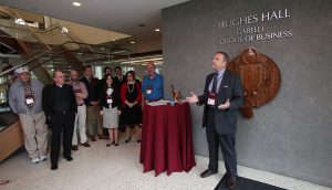 Jack Kawa addresses a group in front of the Hughes Hall signage on the ground floor of Hughes Hall.