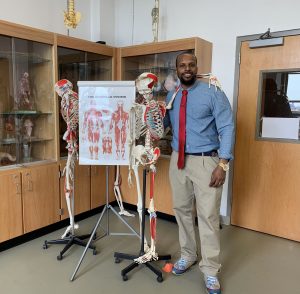 Professor standing next to a skeleton and a diagram.