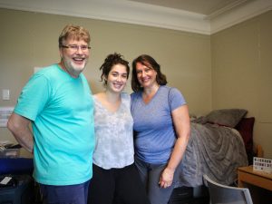 Three people pose for a picture in a dorm room.