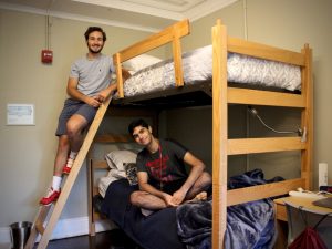 Two boys pose for a photo on a bunk bed.