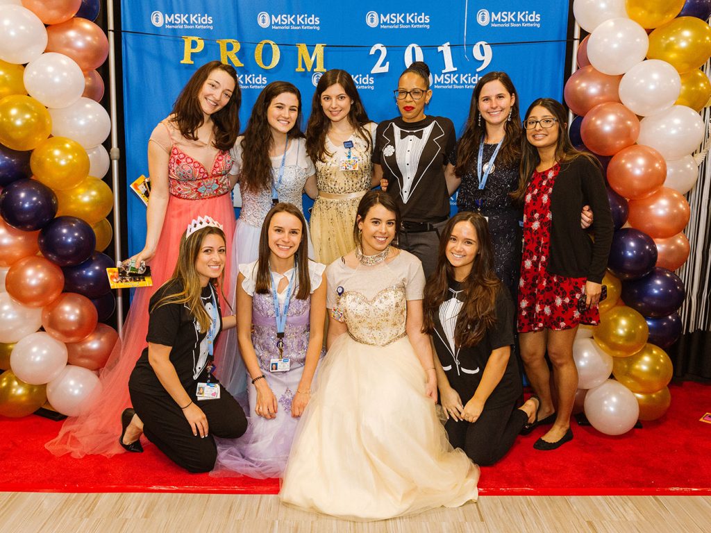 Women pose for a group picture while wearing various colored prom dresses