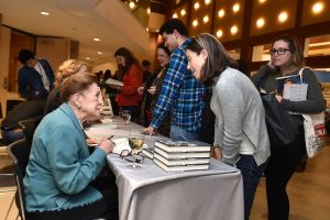 Mary Higgins Clark speaking to a student while seated at a table.