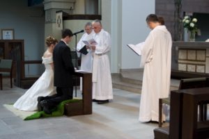 A bride and groom kneeling before men wearing white