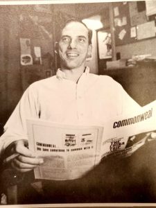 A sepia photo of a man smiling and holding a newspaper