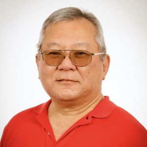 A portrait of a smiling man wearing tinted eyeglasses and a red shirt