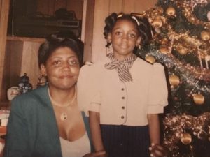 A woman and a girl smile in front of a Christmas tree.