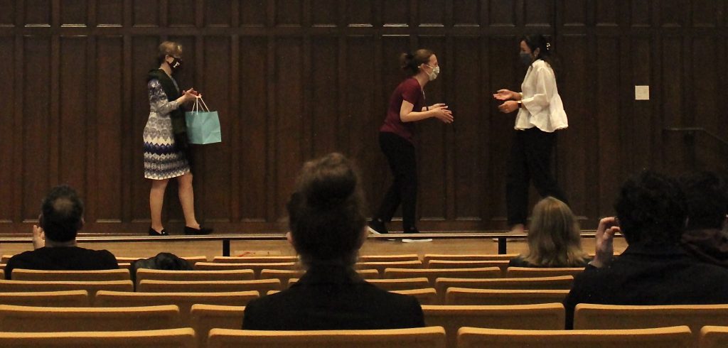 A woman rushes toward another woman for a hug in an auditorium.
