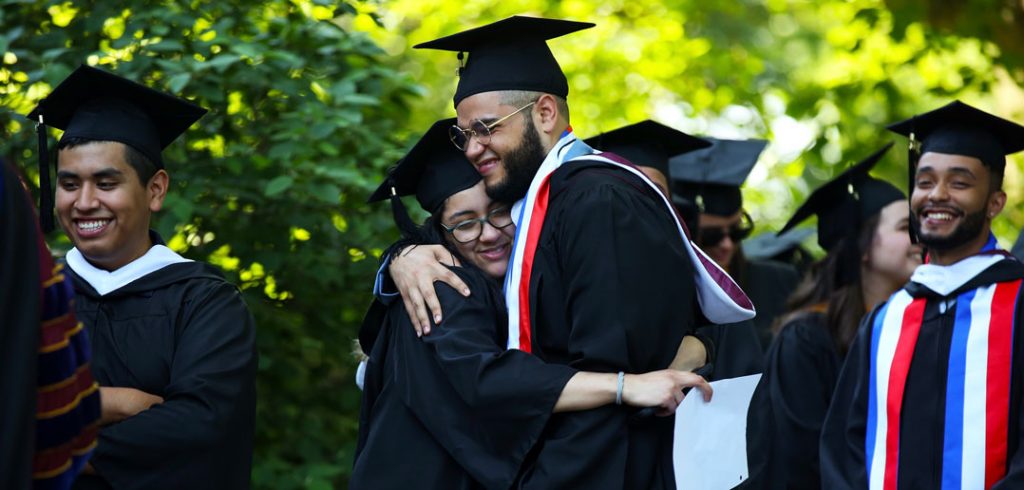A woman and a man wearing black graduation gowns embrace.