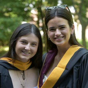 Two women wearing black graduation gowns smile.