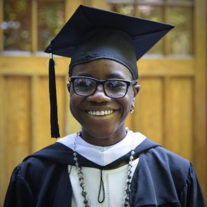A woman wearing glasses and a black graduation cap smiles at the camera.