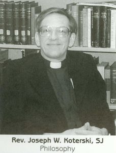 A man wearing glasses and a black Jesuit outfit smiles at the camera.