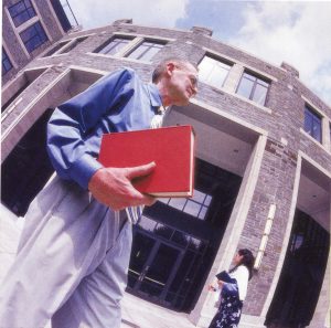 A man holding a red book in front of a large Gothic style building