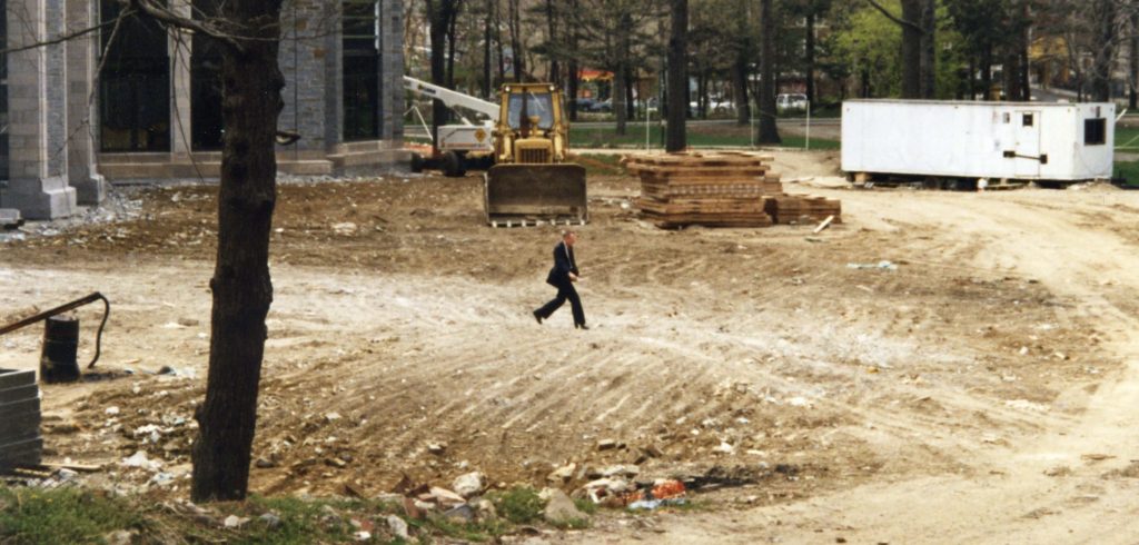 A small man walking along a huge dirt pile in a construction site