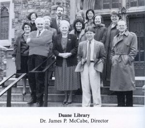 A black-and-white group photo of 13 people standing on the steps of a building