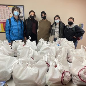 Five masked students stand in front of a group of large plastic bags stuffed with items.