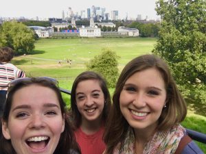 Three girls smile in a selfie against a grassy background.
