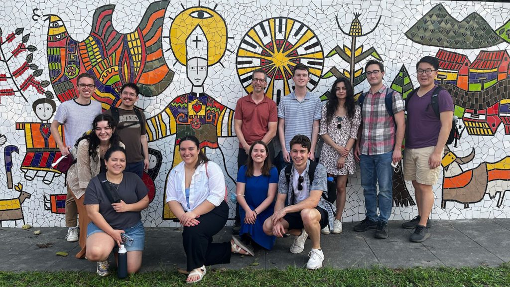 students and faculty stand in front of a mural on a wall in El Salvador